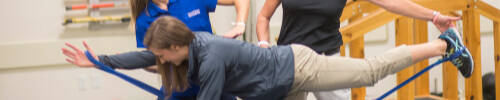 A student performs a stretching exercise with faculty and another student